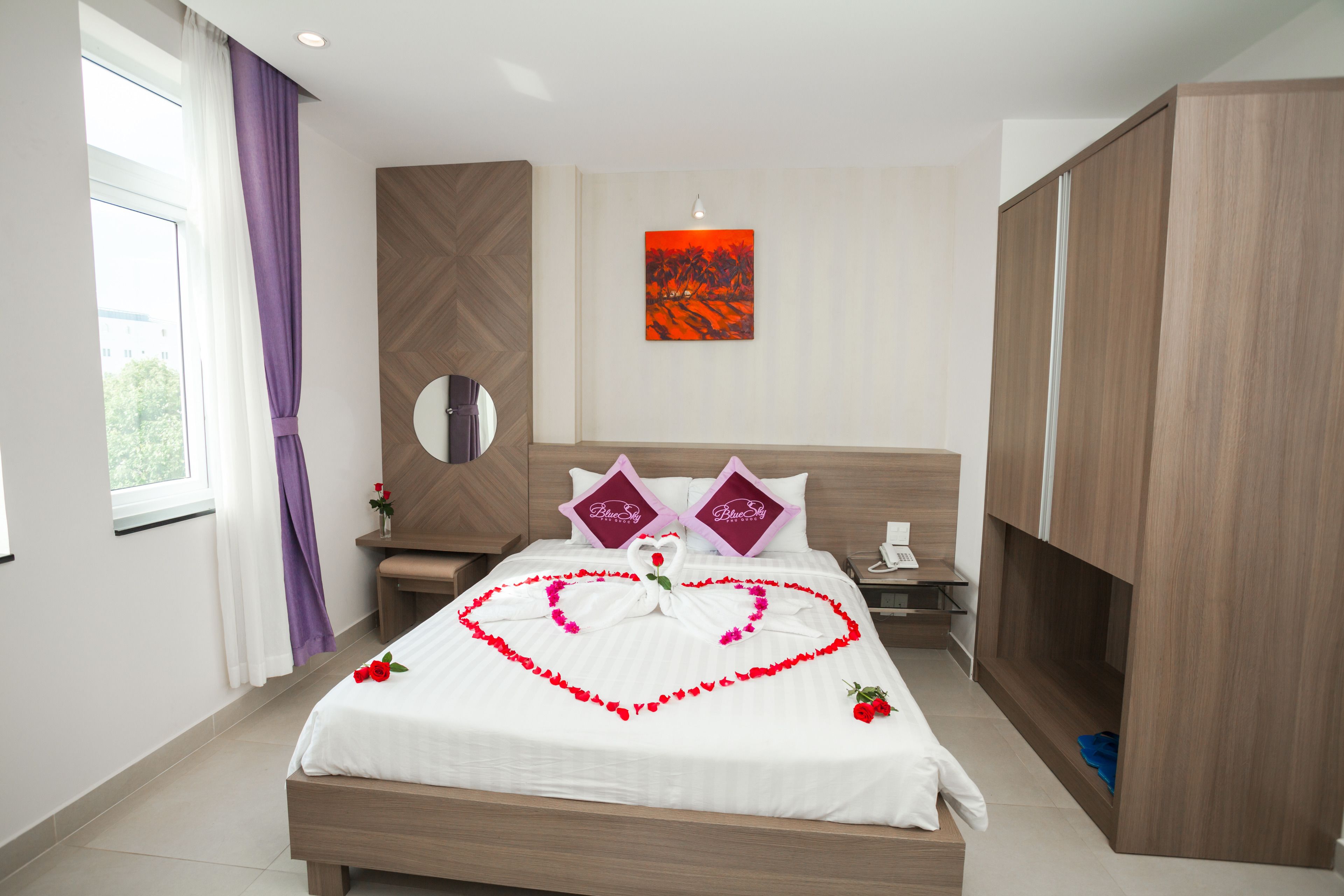 A hotel room with a bed, a nightstand, a mirror, a wardrobe, and a window with curtains.