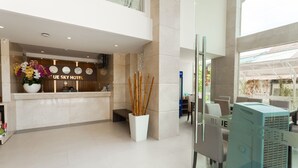 A modern hotel lobby with a reception desk, a large floral arrangement, and a seating area with tables and chairs. - Blue Sky Phu Quoc Hotel (Phu Quoc)