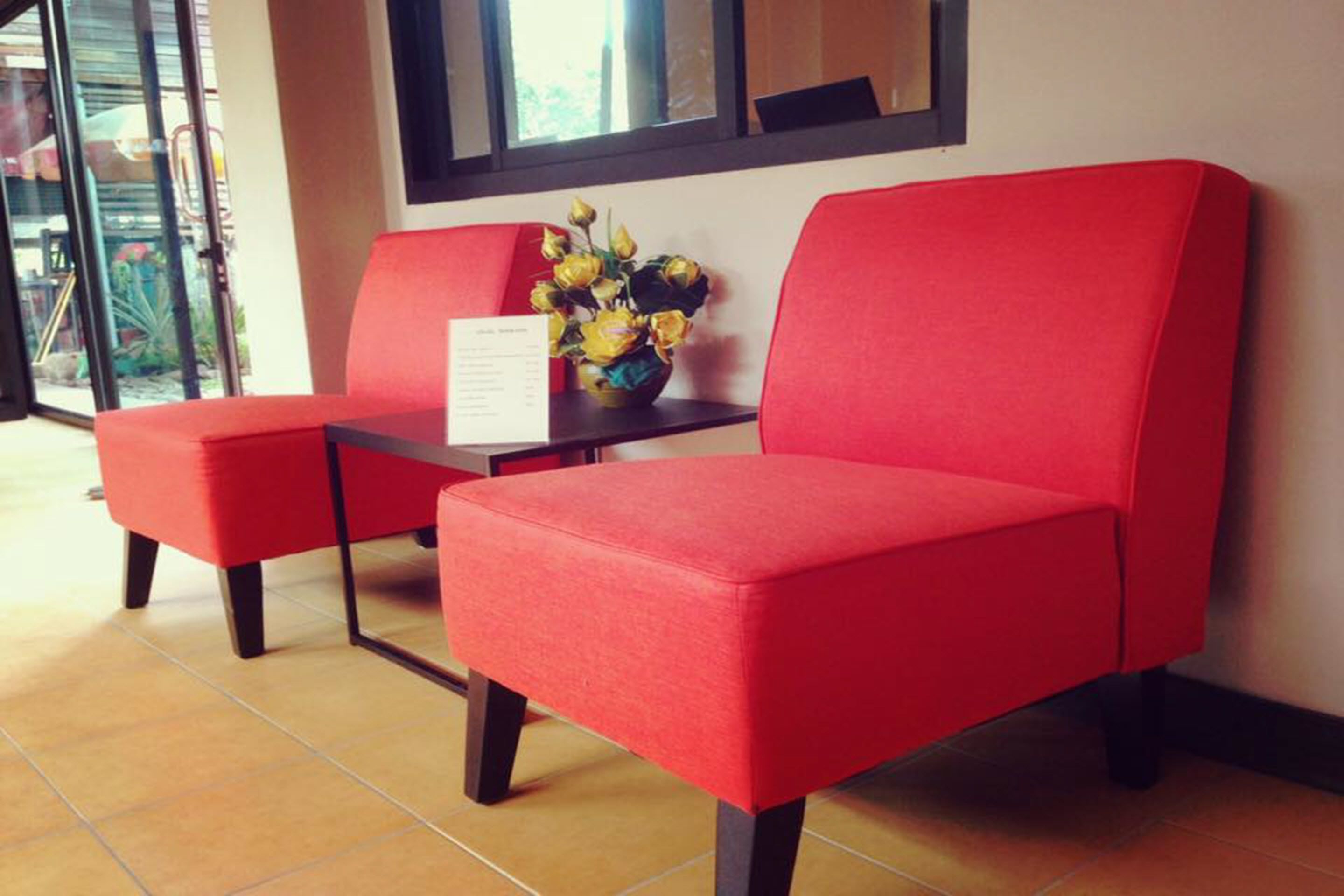 A reception area with two red cushioned chairs, a small table with a vase of yellow flowers, and a window with a view of the outside.