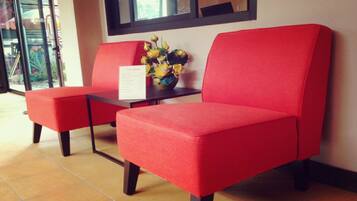 A reception area with two red cushioned chairs, a small table with a vase of yellow flowers, and a window with a view of the outside.
