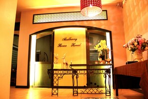 Un espace d’accueil avec une enseigne indiquant « Mulberry House Korat », une rampe décorative en métal et un vase rempli de fleurs.