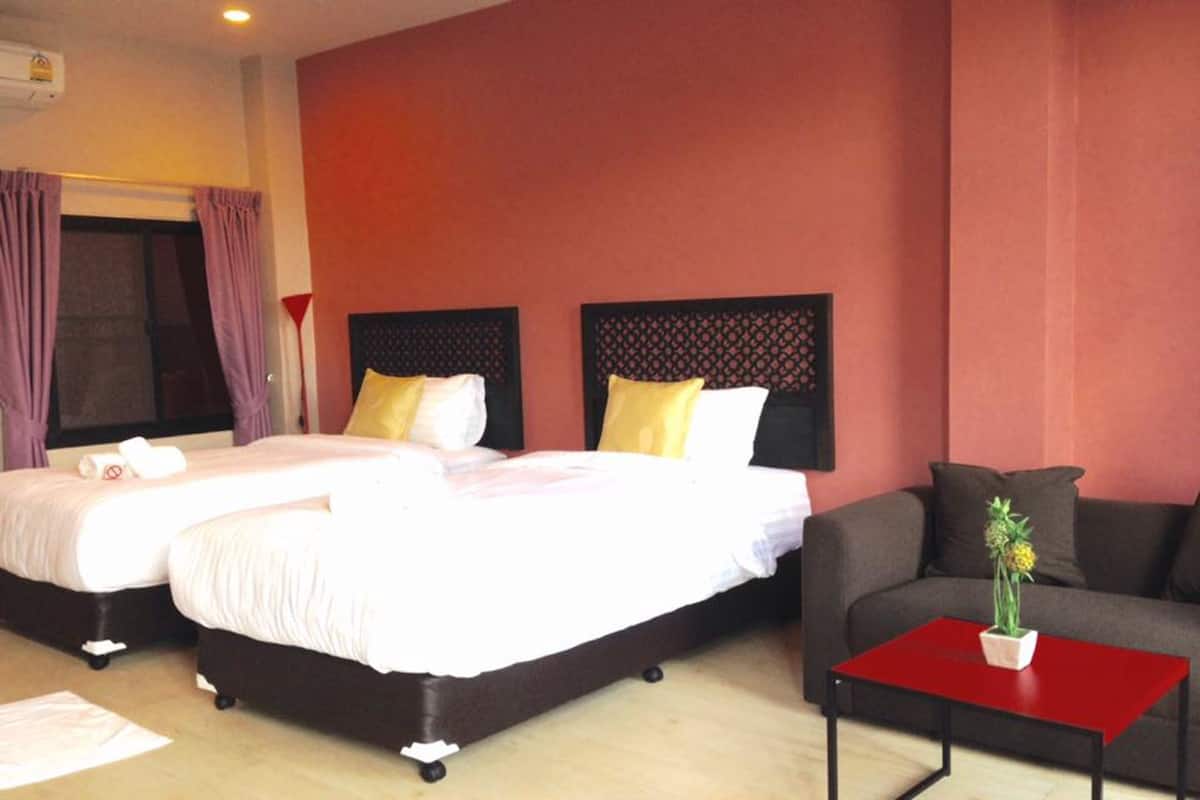 Habitación de hotel con dos camas, un sofá y una pequeña mesa con una planta.