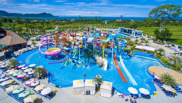 Un parc aquatique doté de nombreux toboggans et de plusieurs piscines, entouré d’installations de plage et offrant une vue sur l’océan.