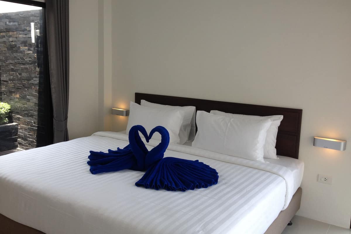 A neatly made bed with white linens and blue towels arranged in a heart shape.