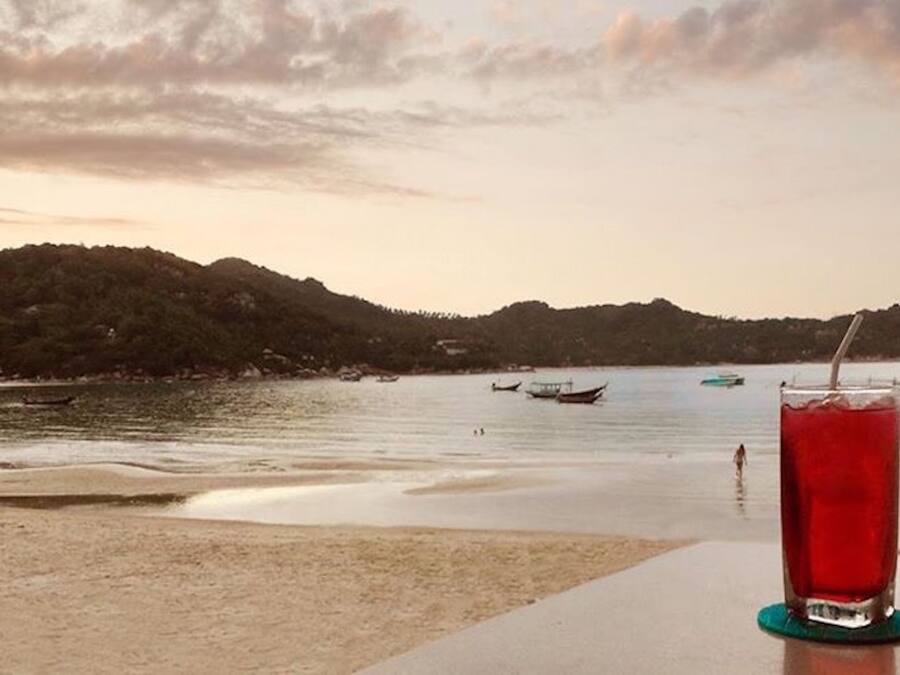 A beach with boats, a glass of red drink, and a view of hills.