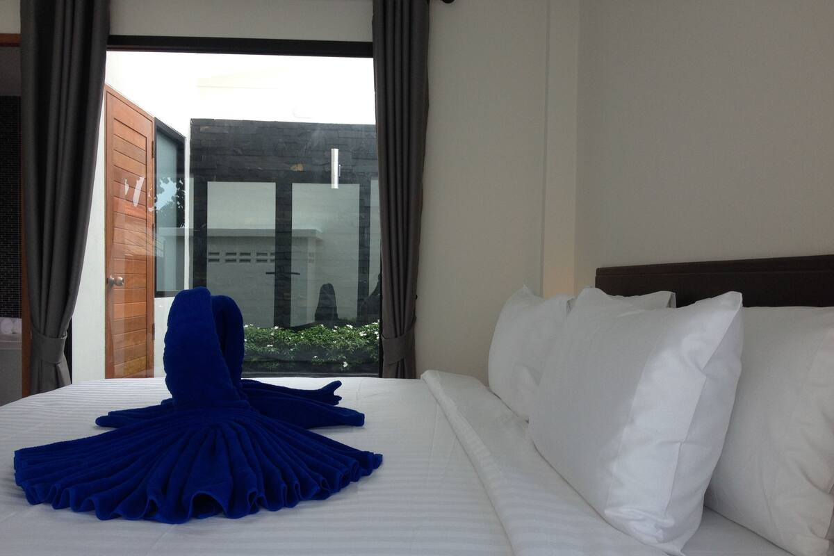A hotel room with a bed, white pillows, and a blue skirt on the bed.