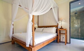 Ein Himmelsbett mit weißer Bettwäsche, ein Nachttisch aus Holz mit einer Lampe und eine Duschkabine mit Glastüren.