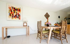 A dining area with a wooden table and chairs, a decorative wall hanging, and a small table with a lamp.
