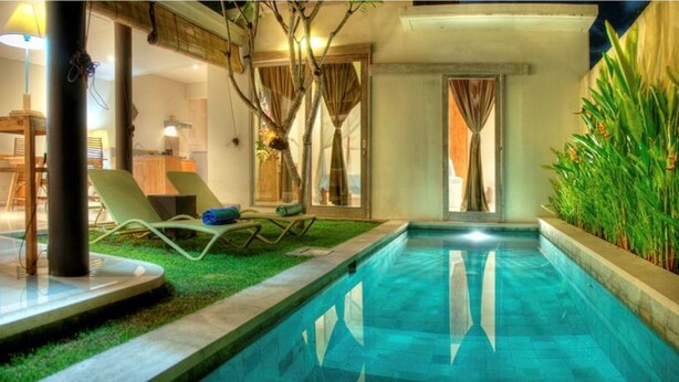 An indoor swimming pool with a small grassy area, a lounge chair, and a view of the outside through a window. - Villa Lestari (Kerobokan)