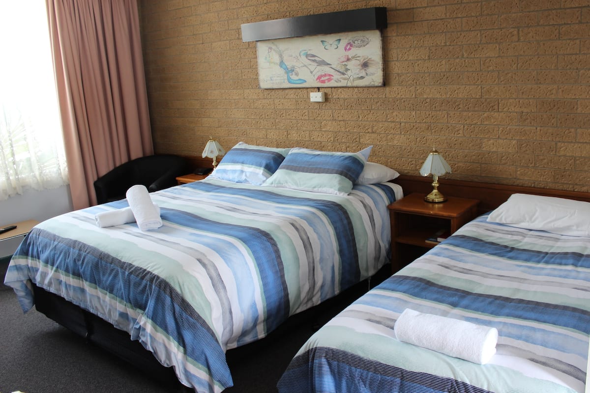A hotel room with two beds, a brick wall, a painting, and a window with curtains.