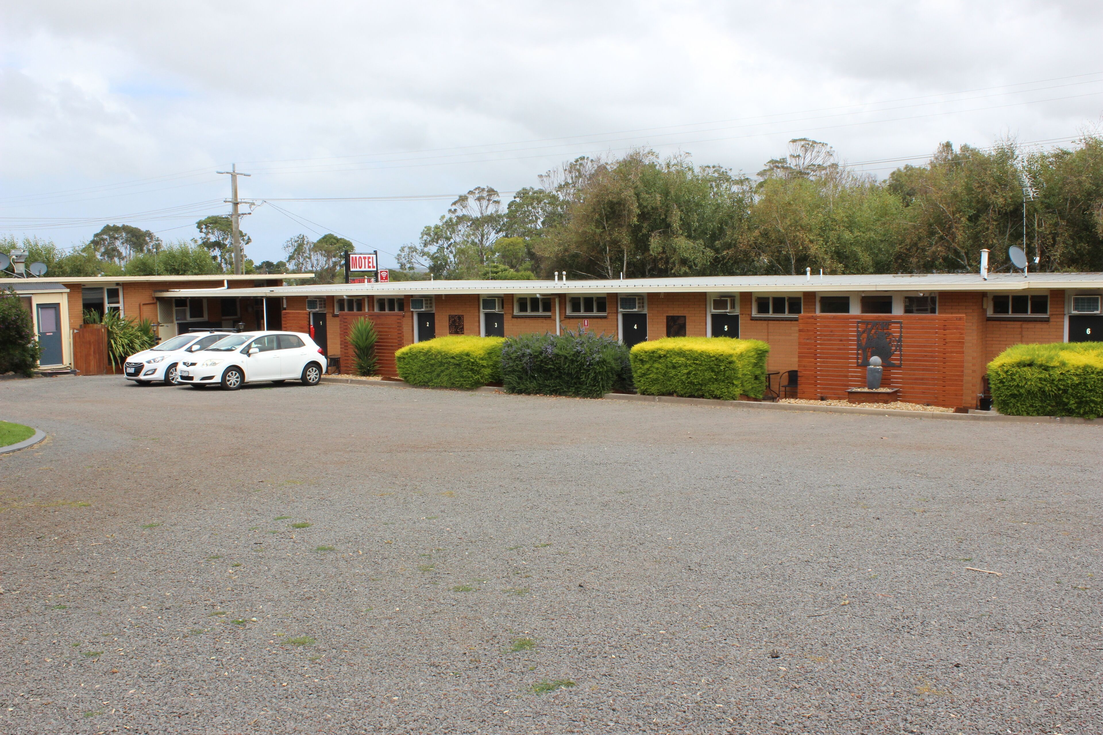 A motel with a brick facade, multiple rooms, and a gravel parking area.