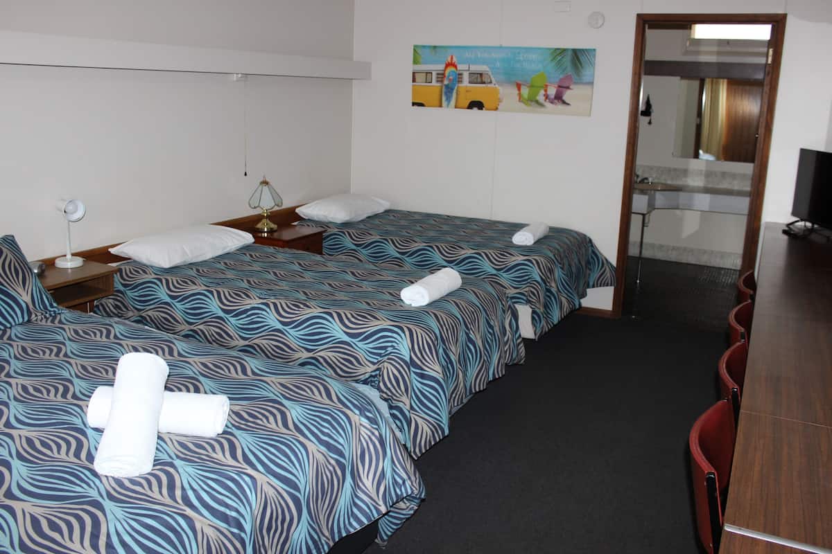 A hotel room with two beds, a desk, a chair, a TV, and a bathroom visible through a glass door.