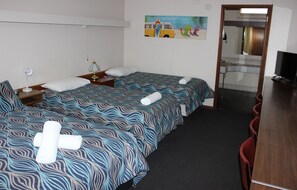 Une chambre d’hôtel avec deux lits, un bureau, une chaise, une télévision et une salle de bain visible à travers une porte en verre.