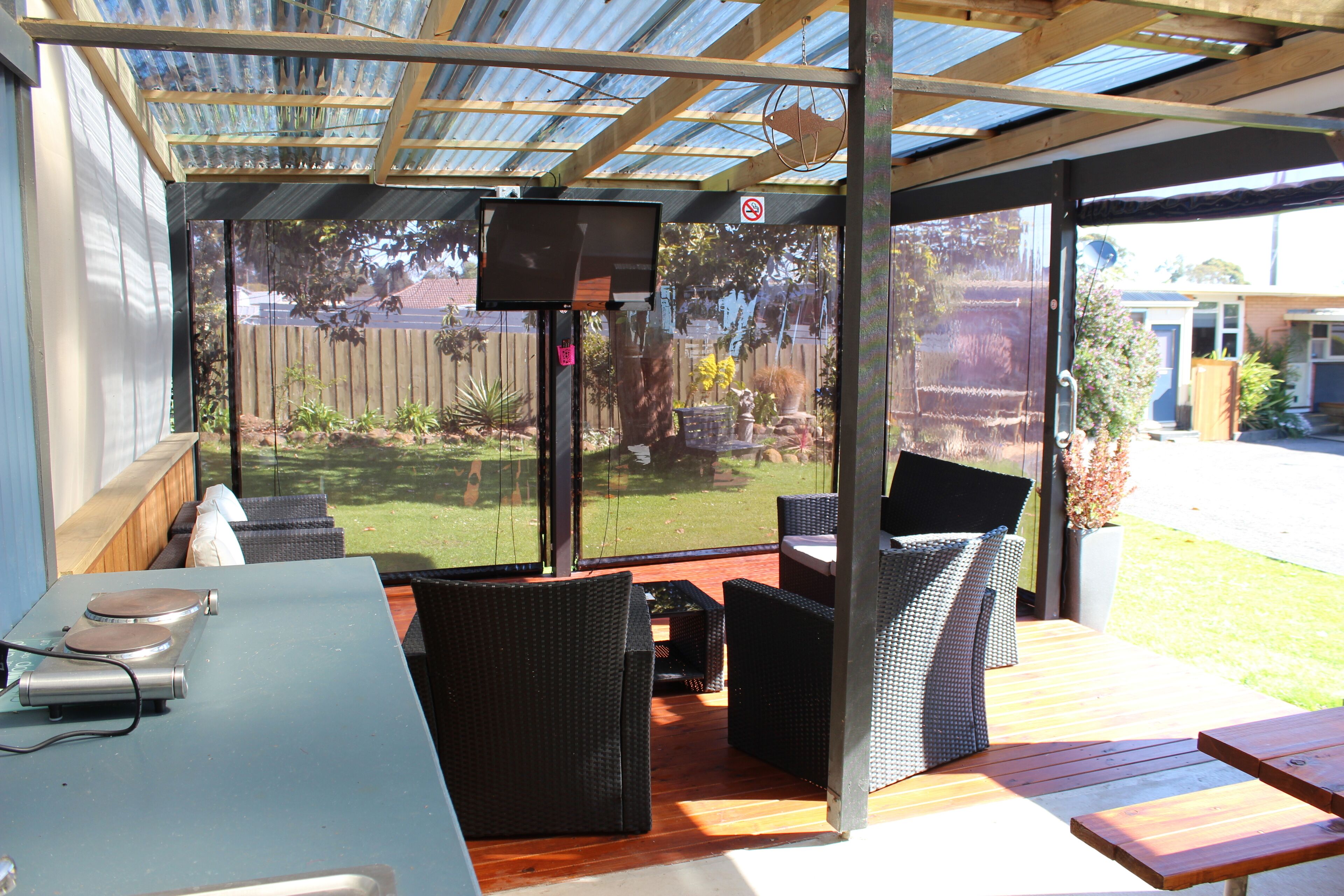 A covered outdoor seating area with wicker furniture, a table with electronic devices, and a view of a backyard.