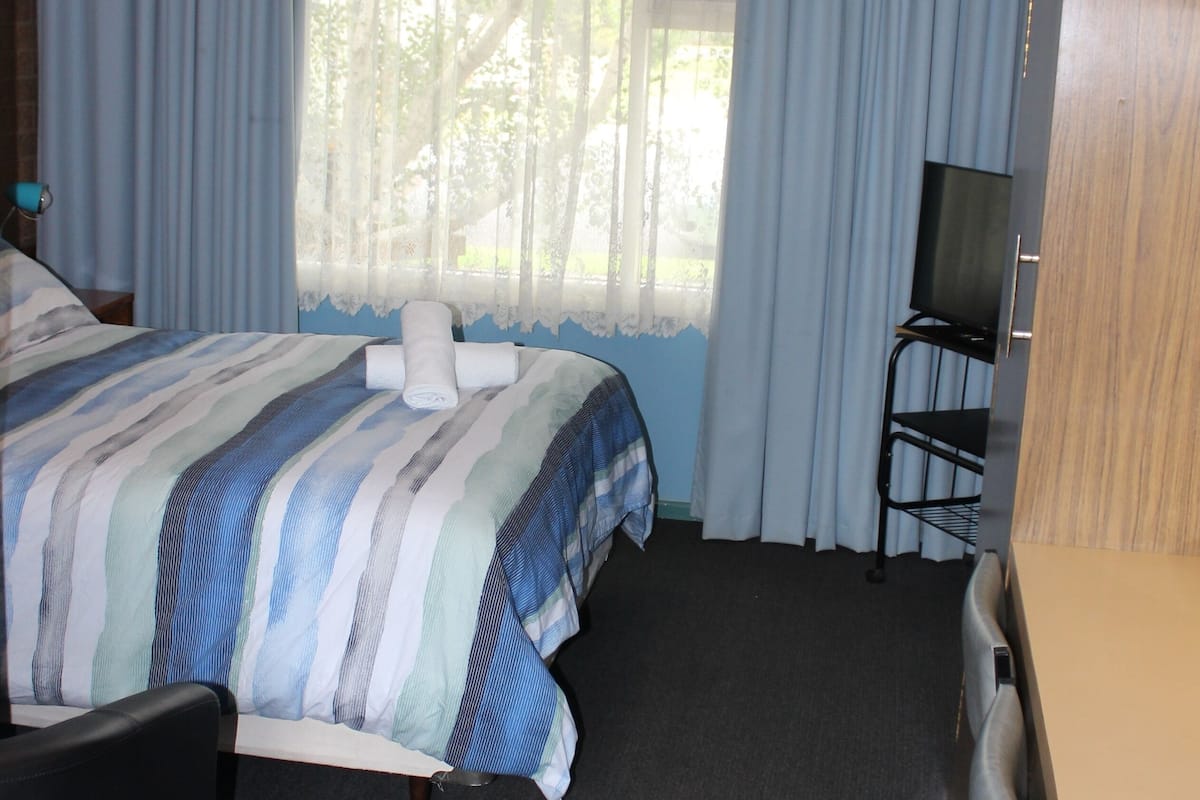 A hotel room with a bed, a desk, a chair, a television, and a window with curtains.