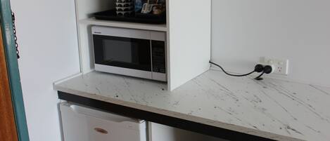 A compact kitchenette with a microwave, a small refrigerator, and a trash bin.