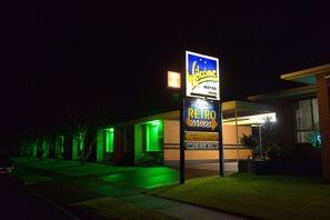 A motel with a neon sign, a green-lit entrance, and a brick facade.