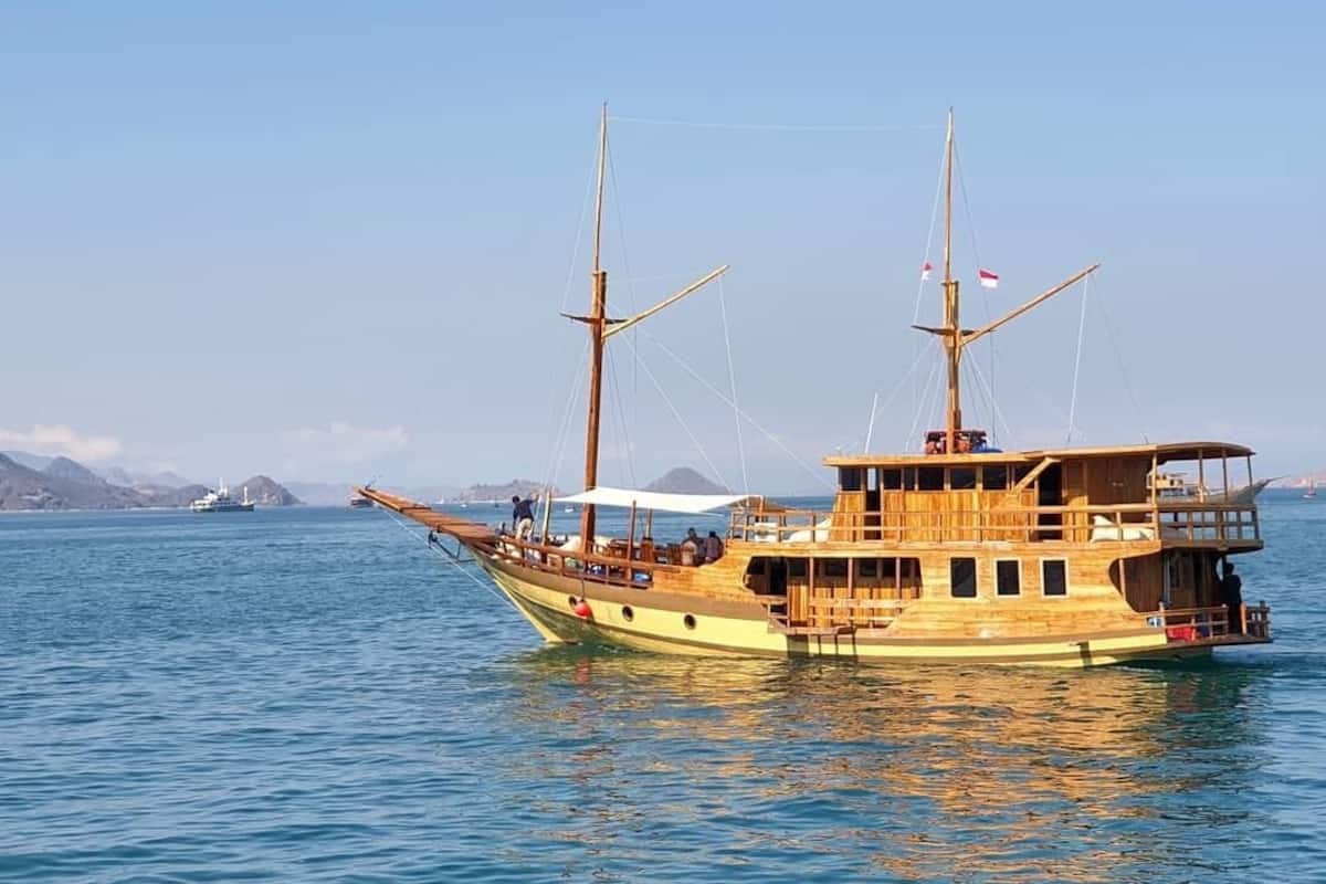 A wooden boat with multiple decks and a cabin structure, floating on calm water.