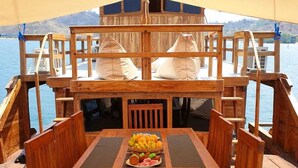A wooden deck with a table set for dining, overlooking a body of water. - Komodo Cruise Boat (Labuan Bajo)