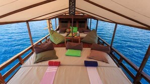 A boat with a covered deck, a table with cushions, and a view of the sea. - Komodo Cruise Boat (Labuan Bajo)