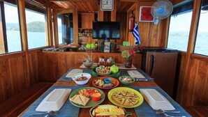 A wooden cabin with a dining table set for a meal, a television, and a fan. - Komodo Cruise Boat (Labuan Bajo)