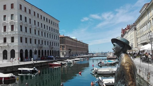 A canal with boats, historic buildings, and a statue. - Brilliant Camere (Trieste)