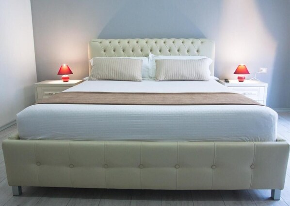 Una cama grande con cabecera capitonada, dos mesitas de noche con lámparas y una paleta de colores neutros.
