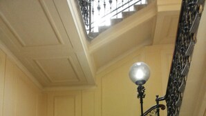 A grand staircase with ornate black balustrades and a large, round wall-mounted light fixture. - Brilliant Camere (Trieste)
