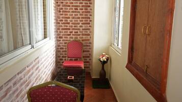 A narrow hallway with a brick wall, a wooden door, a red chair, and a small table with a vase of flowers.