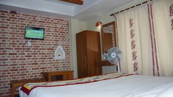 Quarto com parede de tijolos, televisão fixada na parede, guarda-roupa de madeira, mesa de cabeceira com abajur e cama com colcha.