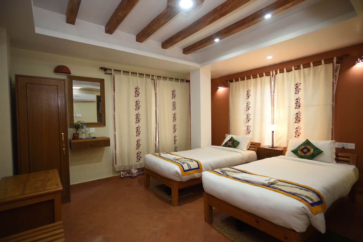 A hotel room with two beds, wooden headboard, a wooden desk, a mirror, and a shelf with a plant.