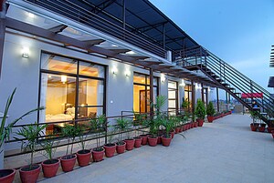 Un hotel moderno con ventanas amplias, un espacio exterior cubierto con plantas en macetas y una escalera que conduce a un nivel superior.