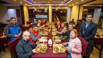 Un grupo de personas sentadas alrededor de una mesa con platos tradicionales, en un comedor interior bien iluminado con un diseño de techo moderno.