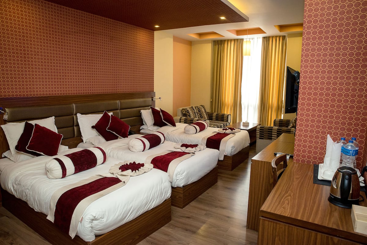 A hotel room with four beds, a wooden desk, a television, and a window with curtains.