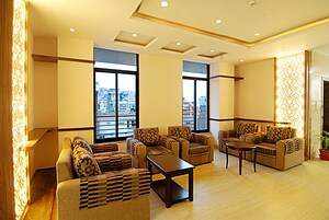 Amplia sala de estar con varios sofás y una mesa de centro, ventanas grandes que ofrecen vistas a la ciudad y un panel decorativo en la pared.