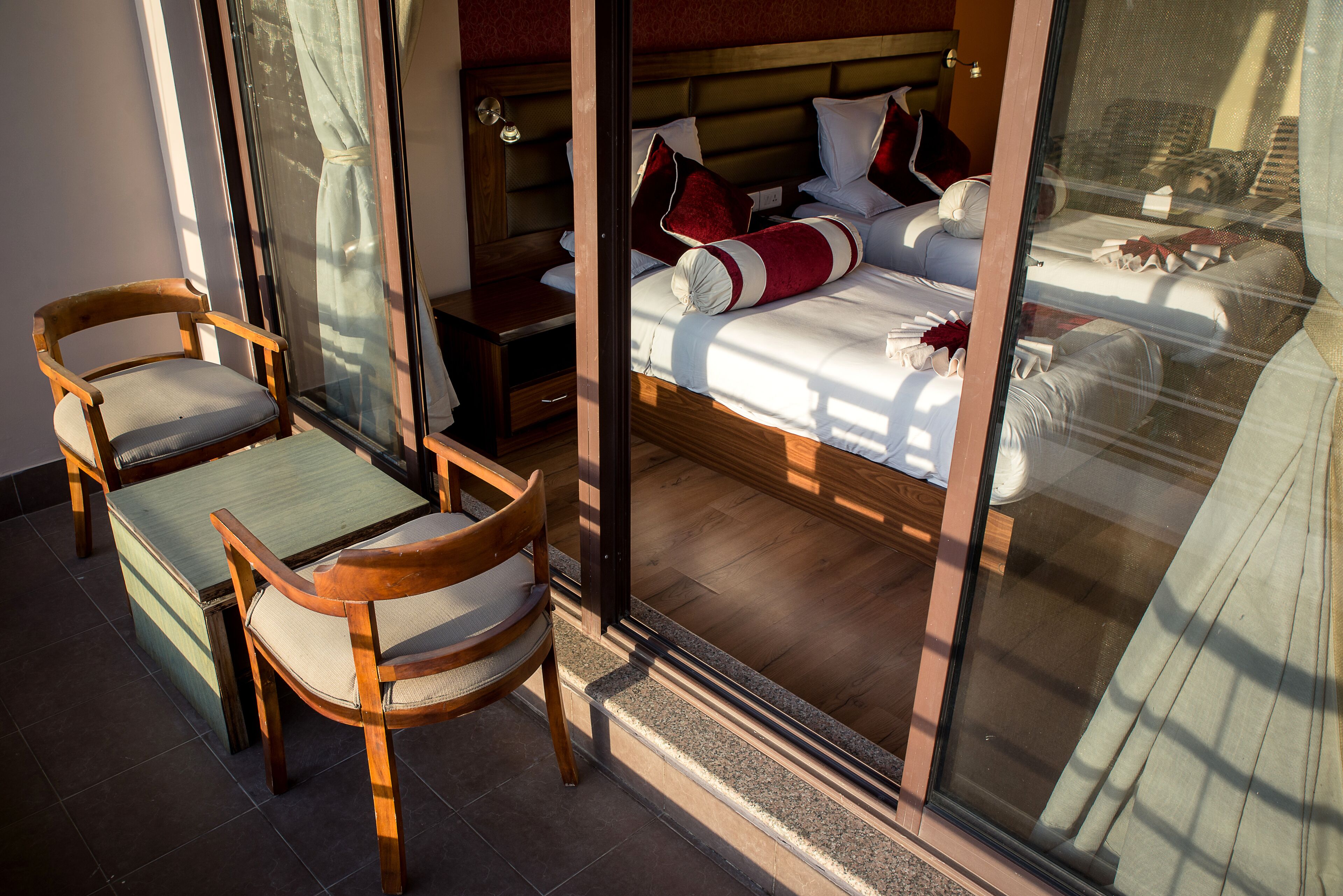 A hotel room with a large bed, two wooden chairs, a small table, and a window with curtains.