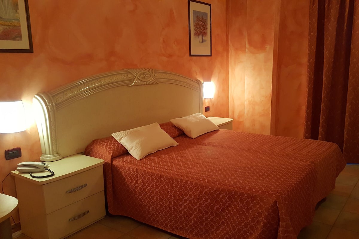 A hotel room with a bed, two bedside lamps, a nightstand, and a drawer unit.