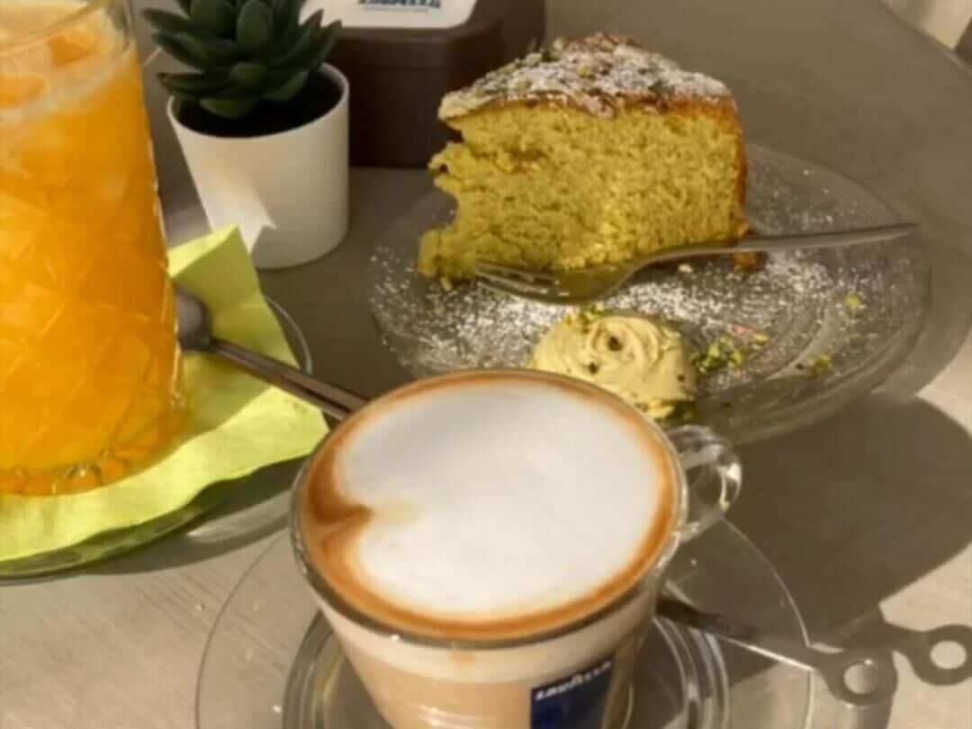 A slice of cake on a plate with a fork, a glass of orange juice, and a cup of coffee on a table.