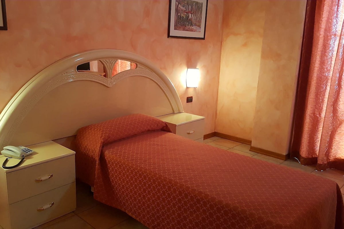 A hotel room with a single bed, a bedside table with a phone, a nightstand with a lamp, and a framed picture on the wall.