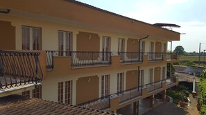 A multi-story building with balconies, a flat roof, and a paved ground area with potted plants. - Hotel Trotter (Leno)