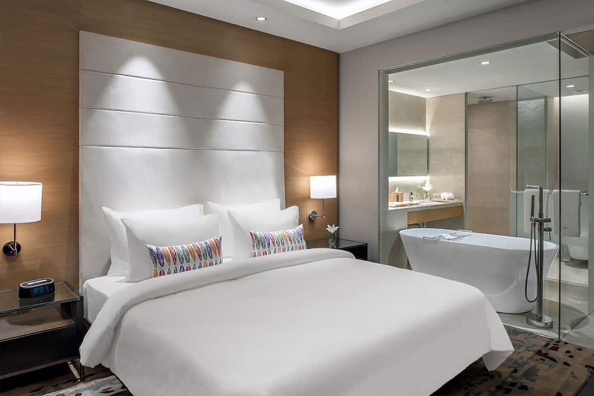 A modern hotel room with a large bed, a glass-enclosed shower, and a nightstand with a lamp.