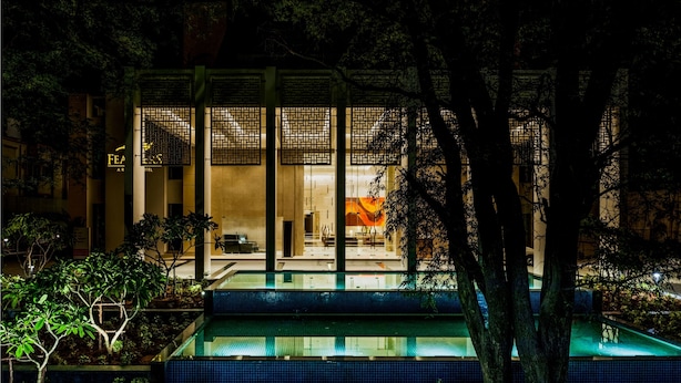 A modern hotel with a pool area, large windows, and a well-lit entrance.