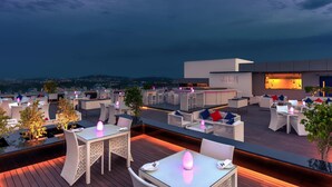 An outdoor terrace with tables and chairs, a bar area, and a view of the cityscape.