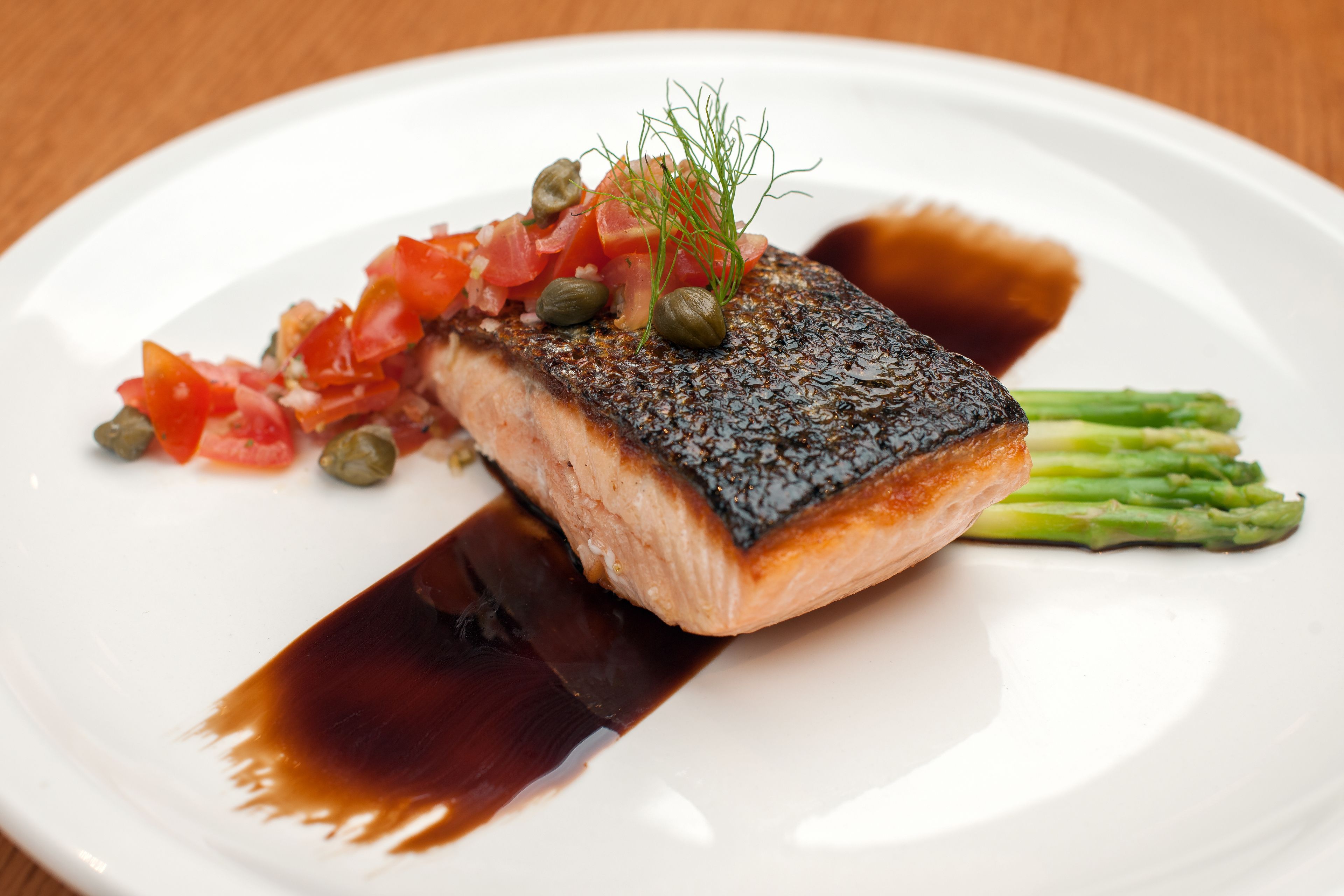 A plate with a piece of salmon, capers, and a garnish of dill.