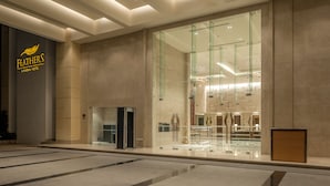 A modern hotel lobby with a glass facade, a reception desk, and a visible elevator.