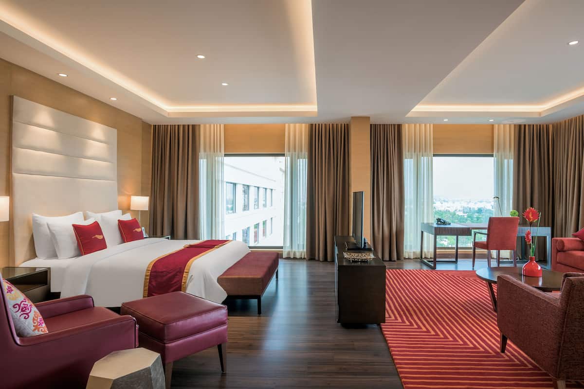 A hotel room with a large bed, red and white decor, a dining area, and a view of the city.