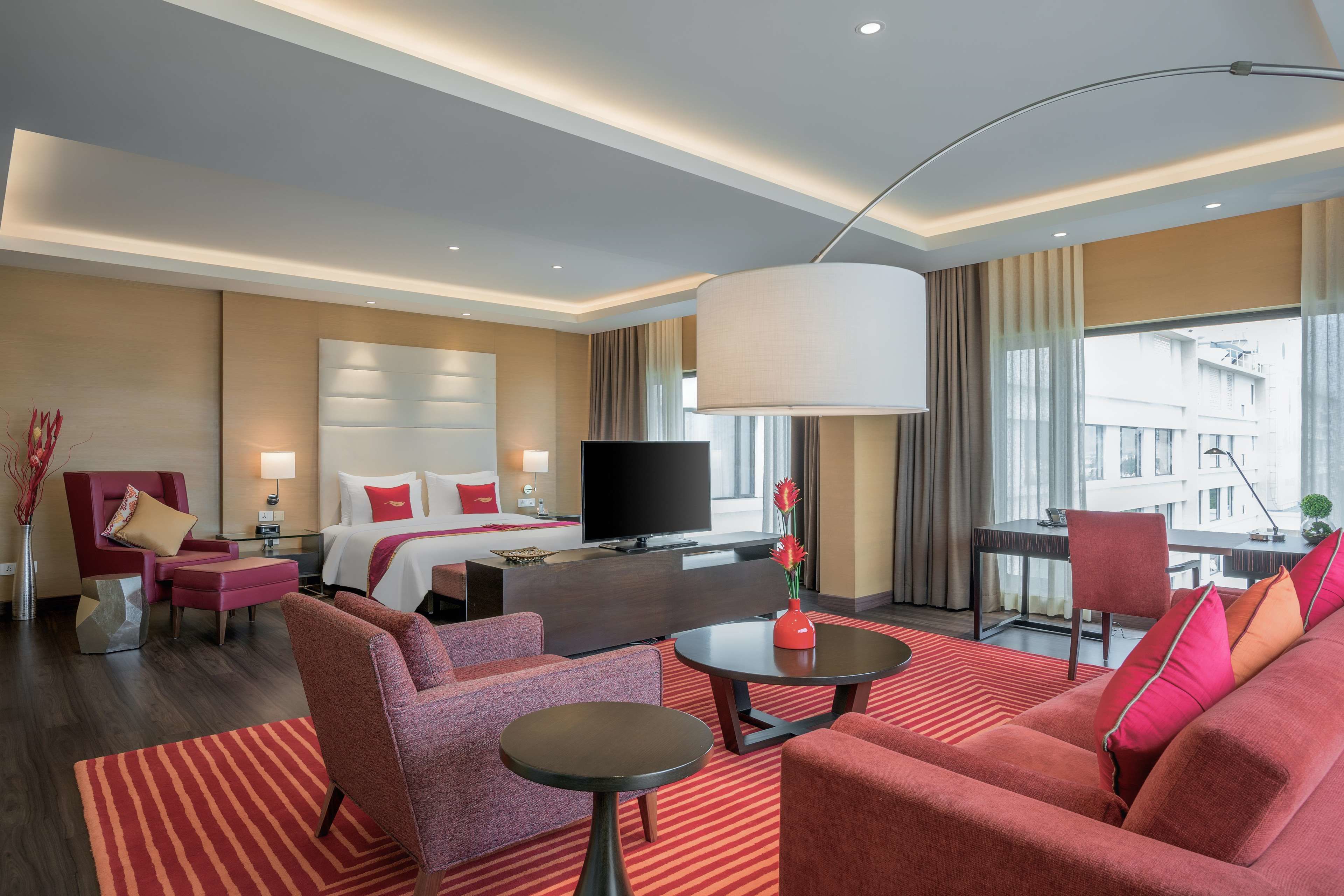 A modern hotel room with a large bed, a TV, a sofa, a coffee table, and a view of the city.