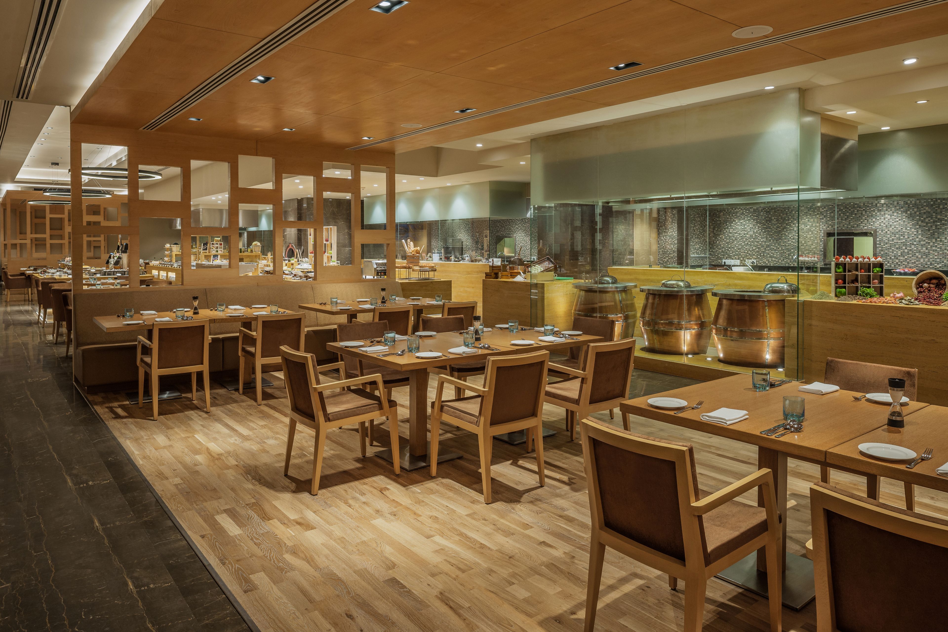 Un restaurante moderno con mesas y sillas de madera, una zona de cocina con electrodomésticos de acero inoxidable y un piso de madera pulida.