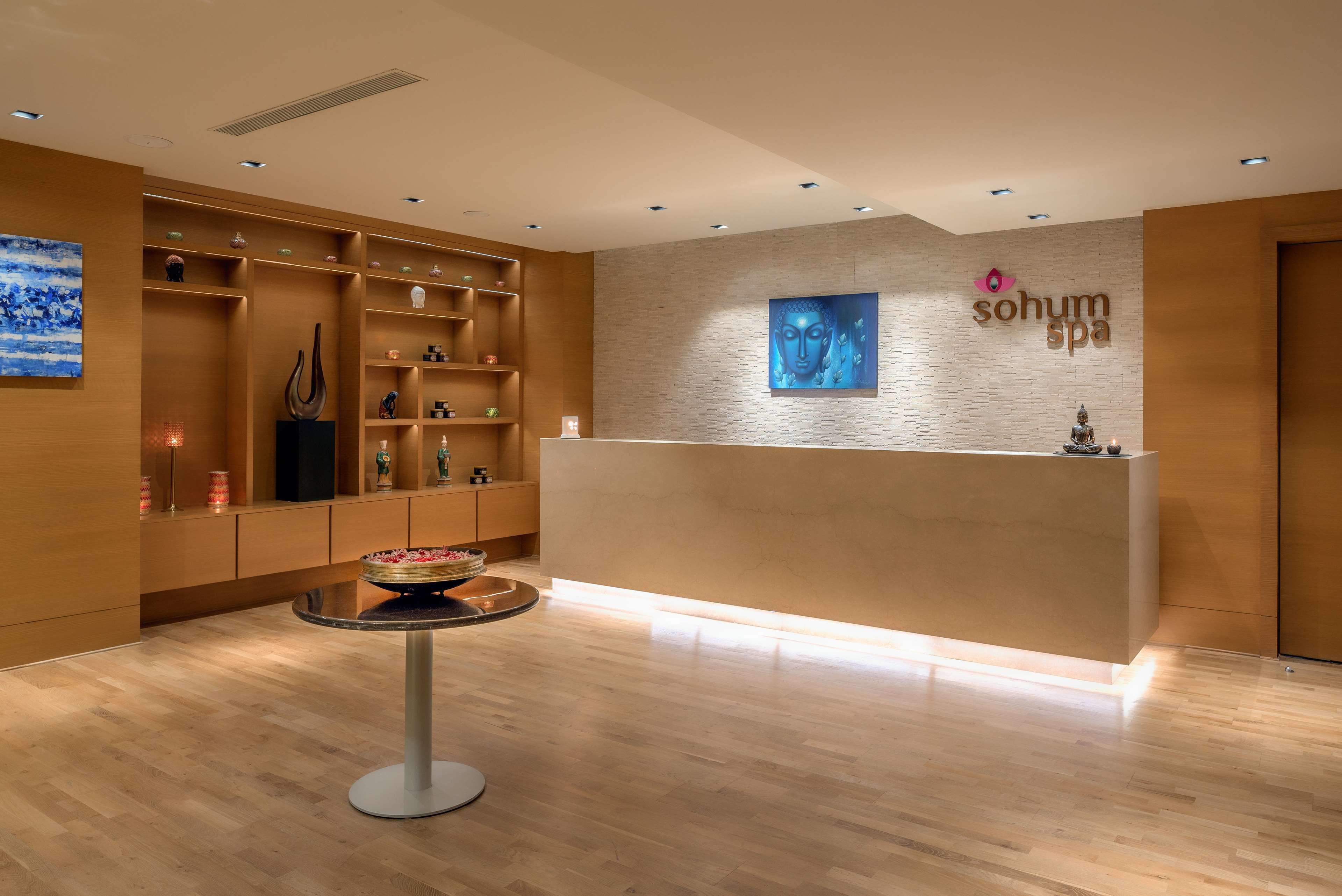 A reception area with a wooden reception desk, shelves with decorative items, and a Buddha statue.