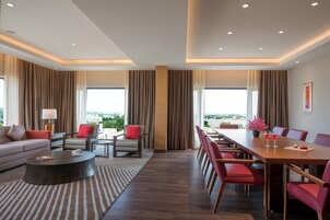 Una habitación de hotel moderna con una amplia mesa de comedor, sillas rojas, un sofá y una mesa de centro.